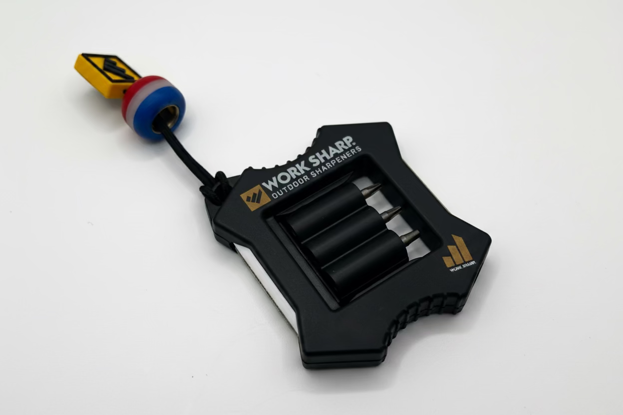 A black Work Sharp outdoor sharpener tool with a small colorful bead keychain attached, photographed on a plain light background.