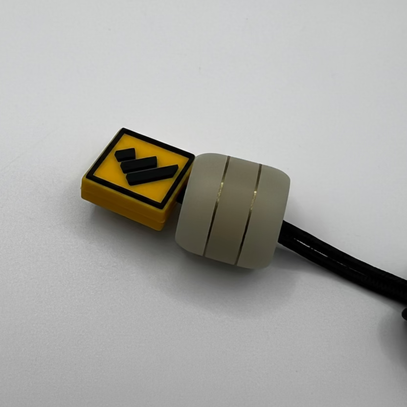 A small automotive sensor or connector component with a yellow warning label, a beige cylindrical body, and a black cable, photographed on a plain light gray background.