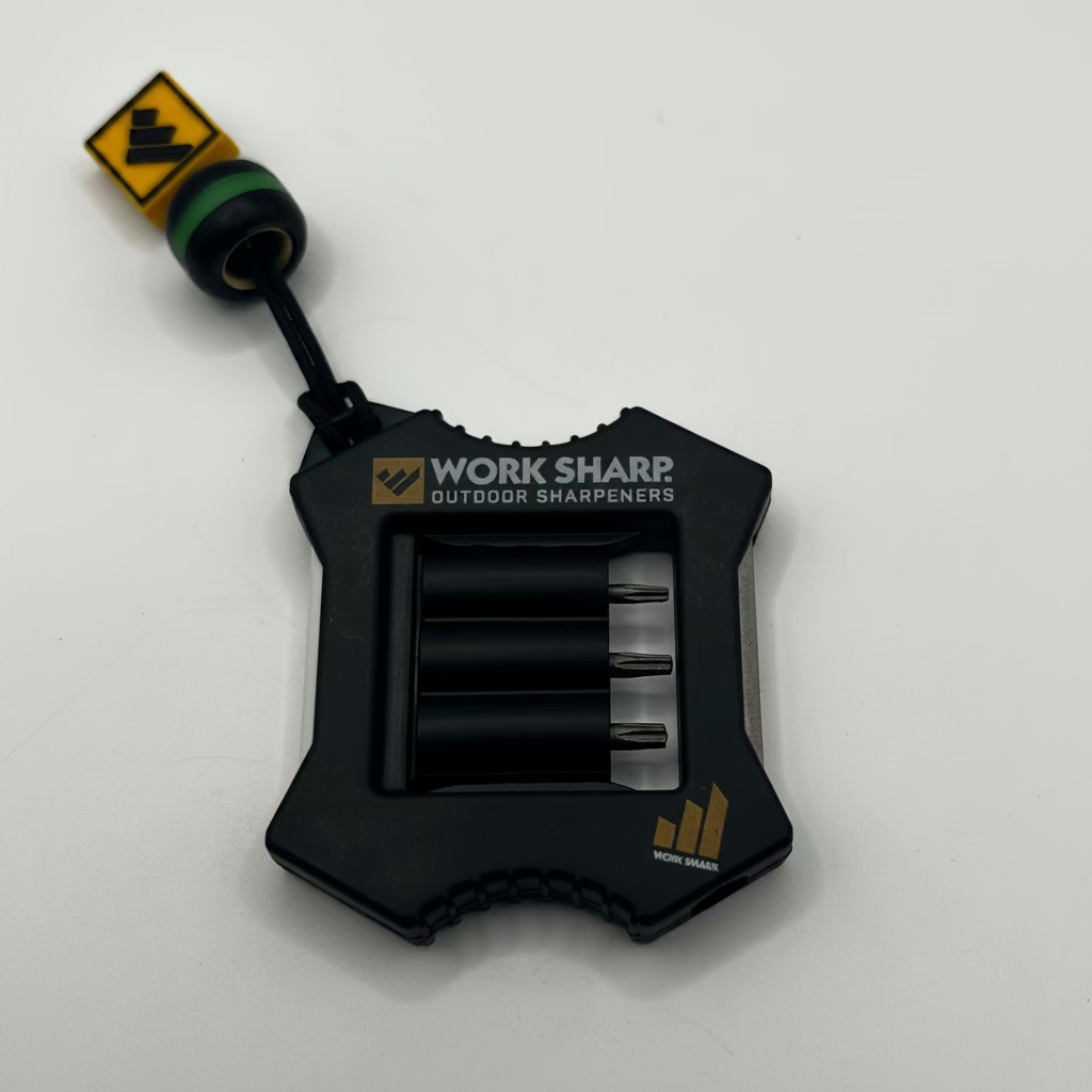 A black Work Sharp outdoor sharpener tool with a lanyard and a small yellow-and-black tag, photographed on a plain light background.